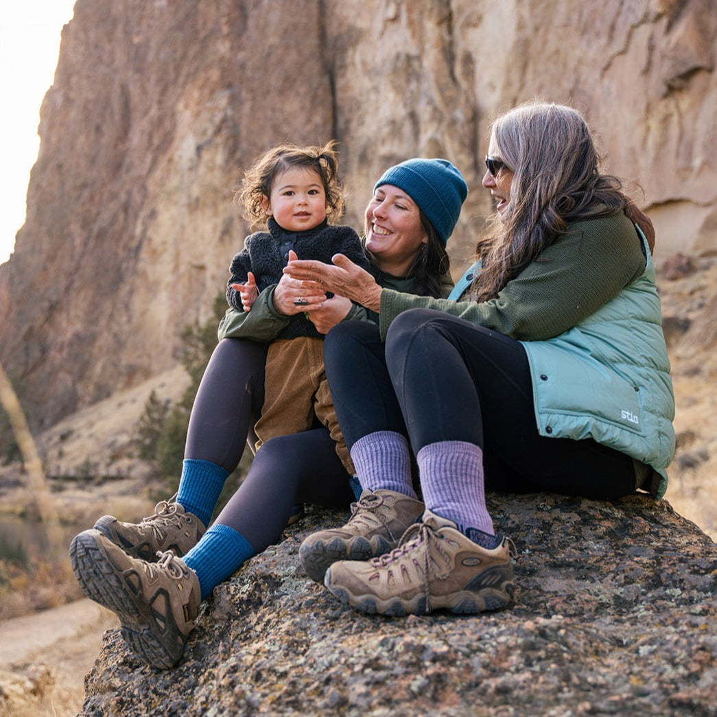 A mom, grandma and baby sit together on a rock in the mountains