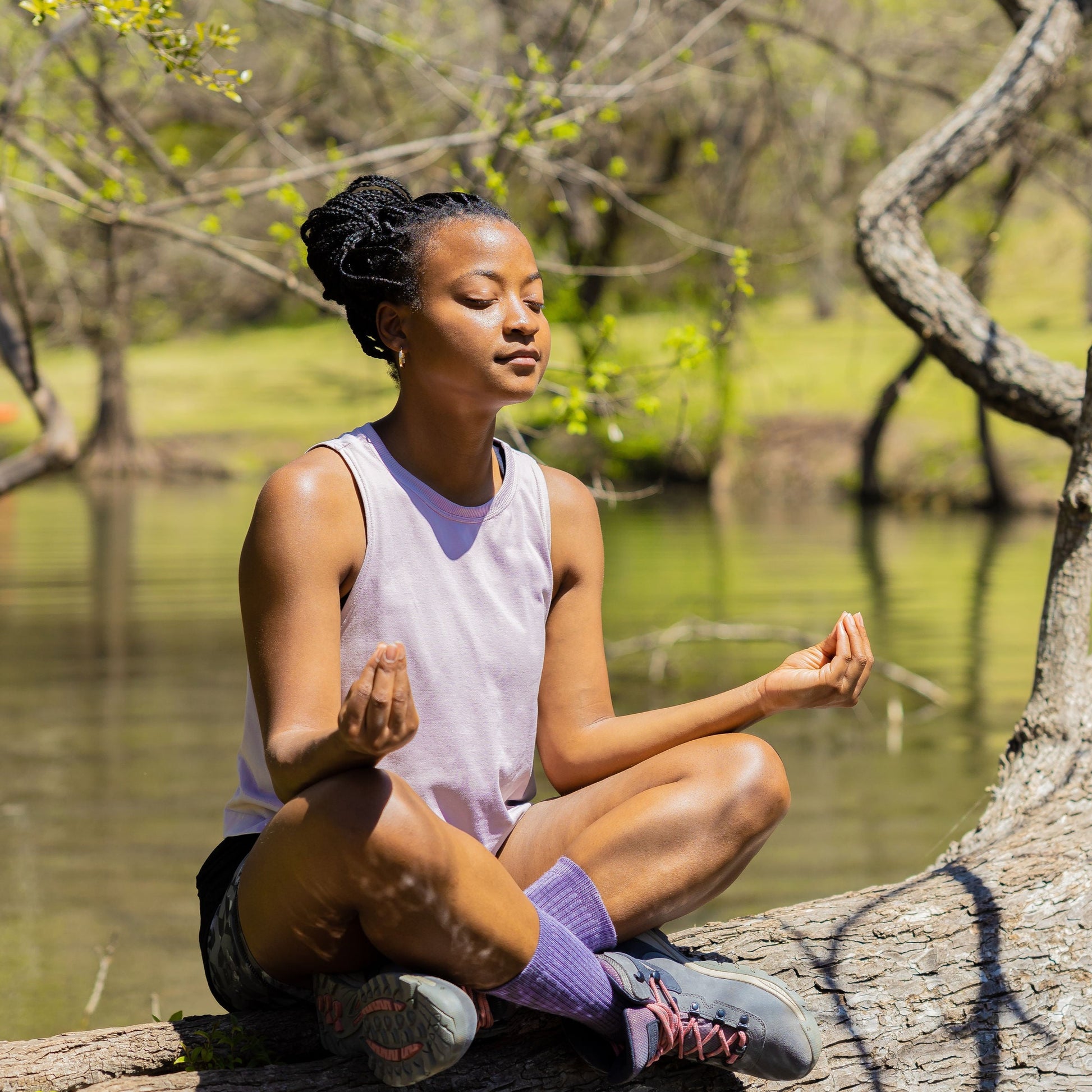 Black woman sitting on a tree branch meditating wearing lavender ToughCutie socks